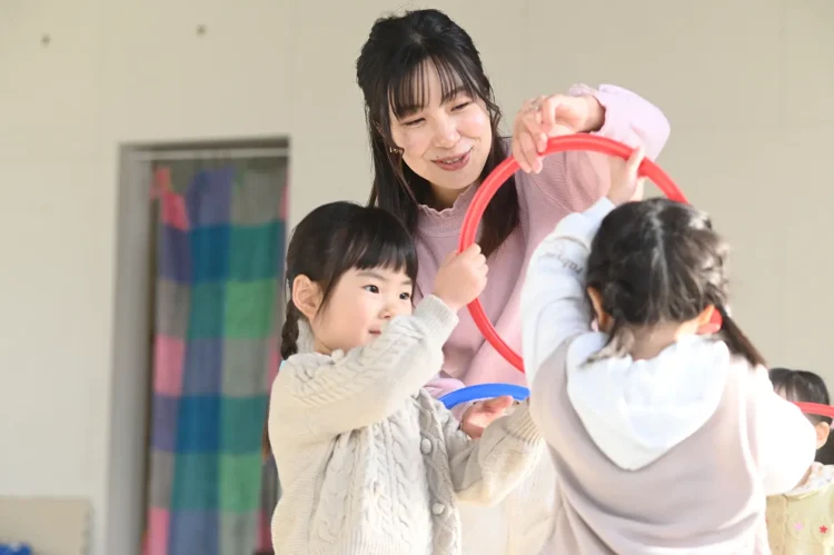 先生と一緒に、輪っかを使って遊んでいる小さな子どもたち